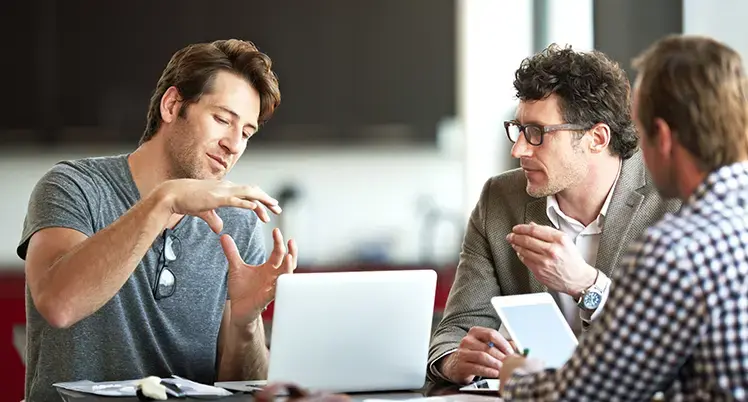 Personer i samtal under ett arbetsmöte vid en laptop